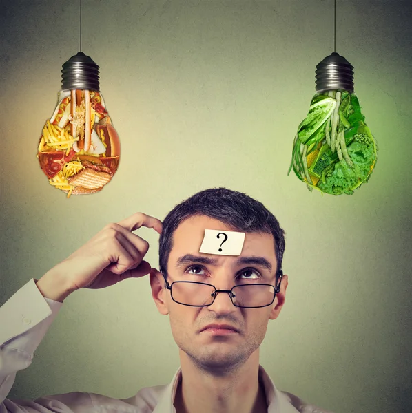 Man with question mark thinking looking up at junk food and vegetables shaped as light bulb — Stockfoto