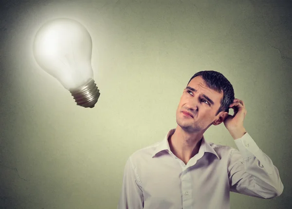 Concerned man thinks looking up at light bulb — Stock Fotó