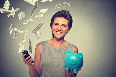 Happy woman with piggy bank and smart phone dollar banknotes bills flying away