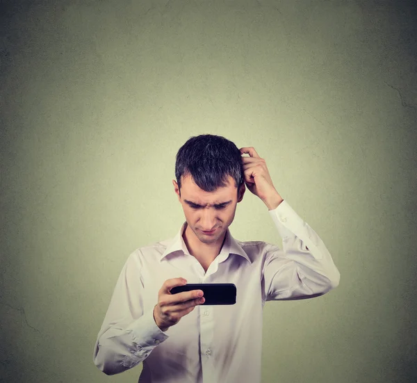 Ratloser junger Mann schaut aufs Handy und sieht schlechte Nachrichten oder Fotos — Stockfoto