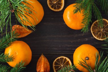 Fresh and dried tangerines with pine and spruce branches, physalis close-up arranged in a frame.