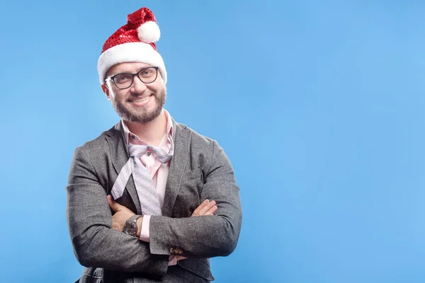 Gri takım elbiseli, beyaz sakallı, pembe tişörtlü, kravat çizgili Noel Baba gülüşlü genç adam açık mavi arka planda mutlu görünüyor. Noel tatili tatili konsepti. Boş metin kopyalama alanı
