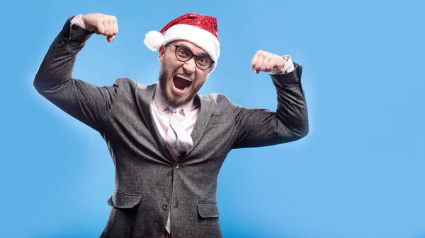 Gri takım elbiseli, beyaz sakallı, pembe tişörtlü, kravat çizgili Noel Baba gülüşlü genç adam açık mavi arka planda mutlu görünüyor. Noel tatili tatili konsepti. Boş metin kopyalama alanı