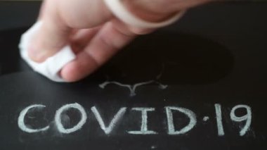 Adamın eli kara tahtadan tebeşirle yazılmış covid-19 kelimesini siliyor. Hijyen ve sağlık konsepti, koronavirüsle mücadele
