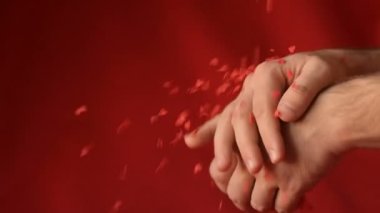 Kırmızı kalp şekeri şekilli konfeti erkeklerin elinde kırmızı arka planda ufalanır ve düşer. Romantik aşk, Sevgililer Günü hazırlık tasarımı konsepti