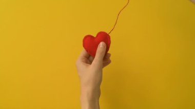 Bir kızın ya da genç bir kadının eli kırmızı keçeli ya da sarı arka planda yünlü kalp diker. Romantik aşk, sevgi dolu Sevgililer Günü, Anneler Günü, düğün hazırlığı tasarım konsepti.