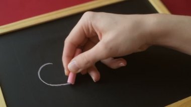 Kız ya da genç bir kadının eli tahtaya pembe tebeşirle kalp hatları çizer. Romantik aşk, sevgi dolu Sevgililer Günü, Anneler Günü, düğün hazırlığı tasarım konsepti.