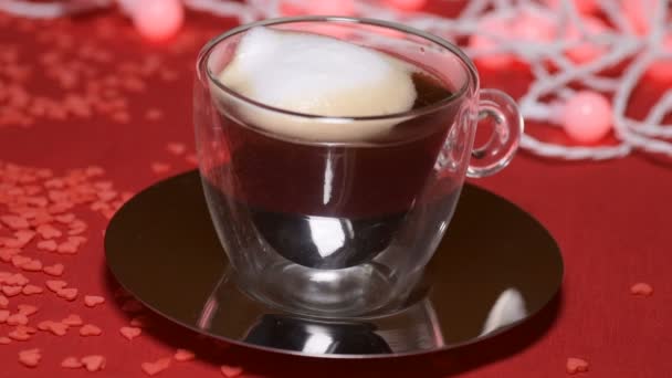 赤いテーブルクロスの鏡板の上の透明ガラスカップにコーヒーを注ぐとカラフルなライトガーランドが点灯 — ストック動画