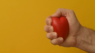 Genç adamın eli kırmızı anti-stres kalp oyuncağını sıkıyor. Romantik aşk, sakinlik ve barış, Sevgililer Günü hazırlık konsepti. Bağış için hazırlık