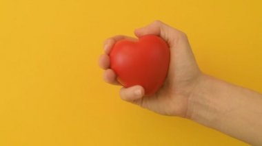 Bir kızın ya da genç bir kadının eli stres önleyici kırmızı bir kalp oyuncağı sıkar. Romantik aşk, sakinlik ve barış, Sevgililer Günü hazırlık konsepti. Bağış için hazırlık