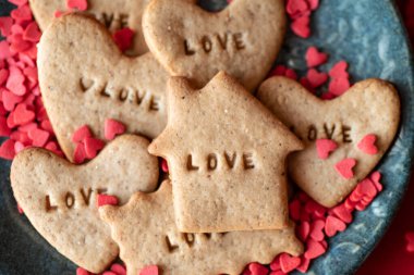 Kırmızı kalpli yeşil tabak ve aşk harfli zencefilli kurabiyeler kırmızı masa örtüsünde duruyor. Aşk, şefkat ve Sevgililer Günü, Anneler Günü, düğün hazırlığı tasarım konsepti.