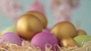 Pembe, altın ve yeşil renkte renkli Paskalya yumurtaları pembe ve mor sümbül çiçekleriyle bulanık yeşil arka planda dönen samanların üzerinde yatar. Bahar Hıristiyan bayramı tasarım konsepti