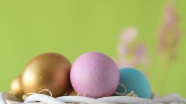 Pembe, altın ve yeşil renkte renkli Paskalya yumurtaları pembe ve mor sümbül çiçekleriyle bulanık yeşil arka planda dönen samanların üzerinde yatar. Bahar Hıristiyan bayramı tasarım konsepti