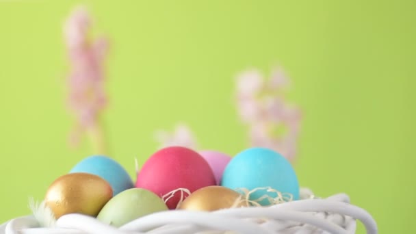 ピンク 緑の色のイースターの卵は ピンクとマゼンタのヒヤシンスの花とぼやけた薄緑色の背景に回ってわらに横たわっています 春キリスト教の休日のデザインコンセプト — ストック動画