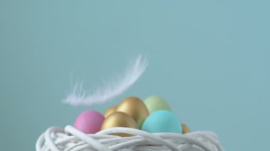 Renkli paskalya yumurtalarının üstüne tüy düşüyor. Pembe, altın ve yeşil renkli renkli yumurtalar bulanık açık yeşil arka planda yatar. Yukarıdan bir tüy düşüyor. Bahar Hıristiyan bayramı tasarım konsepti