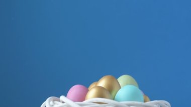 Renkli paskalya yumurtalarının üstüne tüy düşüyor. Pembe, altın ve yeşil renkli renkli yumurtalar bulanık açık yeşil arka planda yatar. Yukarıdan bir tüy düşüyor. Bahar Hıristiyan bayramı tasarım konsepti