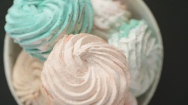 Tatlı renkli ev yapımı pastel şekerlemeler nane yeşili, pembe ve krema renkleri seramik plaka üzerinde ağır çekimde dönüyor sarı arka planda şeker tozu serpiştiriliyor. Yukarıdan görüntüle