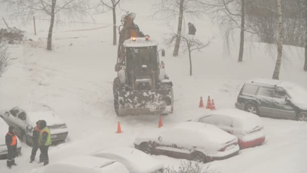 雪から吹雪まで家の間の道路を清掃するトラクター 掘削機車は市内の大きな雪のドリフトをきれいにします ユーティリティサービスの動作 — ストック動画