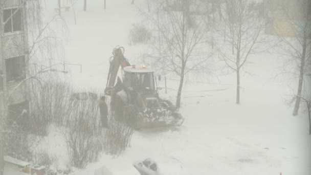 雪から吹雪まで家の間の道路を清掃するトラクター 掘削機車は市内の大きな雪のドリフトをきれいにします ユーティリティサービスの動作 — ストック動画