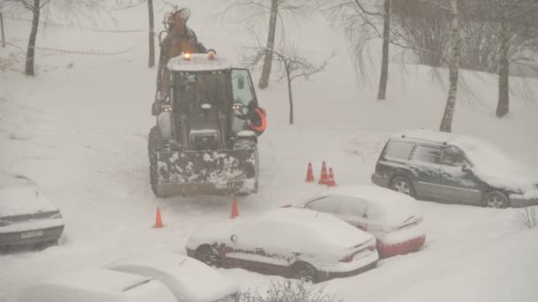 雪下和暴风雪期间拖拉机在房屋之间清扫街道 挖掘机车辆清理了城市里的大雪堆 公用事业工作 — 图库视频影像