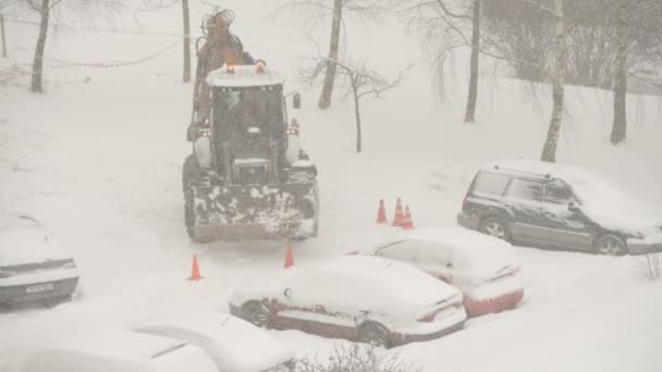 雪下和暴风雪期间拖拉机在房屋之间清扫街道 挖掘机车辆清理了城市里的大雪堆 公用事业工作 — 图库视频影像