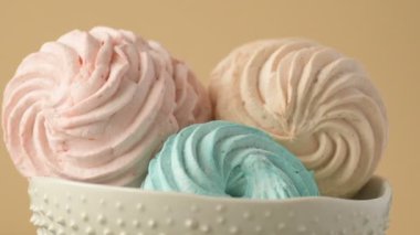 Tatlı renkli ev yapımı pastel şekerlemeler nane yeşili, pembe ve krema renkleri seramik plaka üzerinde ağır çekimde dönüyor sarı arka planda şeker tozu serpiştiriliyor. Ev yemeği. 