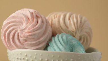Tatlı renkli ev yapımı pastel şekerlemeler nane yeşili, pembe ve krema renkleri seramik plaka üzerinde ağır çekimde dönüyor sarı arka planda şeker tozu serpiştiriliyor. Ev yemeği. 
