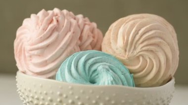 Tatlı renkli ev yapımı pastel şekerlemeler nane yeşili, pembe ve krema renkleri seramik plaka üzerinde ağır çekimde dönüyor sarı arka planda şeker tozu serpiştiriliyor. Ev yemeği. 