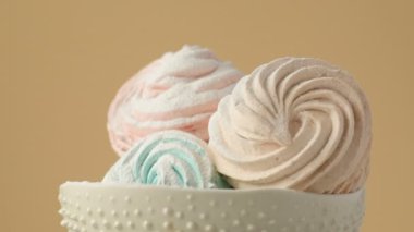 Tatlı renkli ev yapımı pastel şekerlemeler nane yeşili, pembe ve krema renkleri seramik plaka üzerinde ağır çekimde dönüyor sarı arka planda şeker tozu serpiştiriliyor. Ev yemeği. 