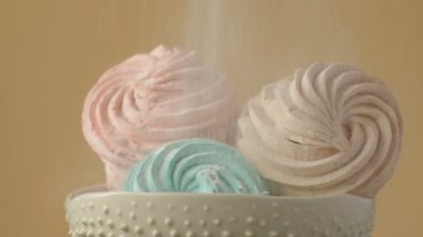 Tatlı renkli ev yapımı pastel şekerlemeler nane yeşili, pembe ve krema renkleri seramik plaka üzerinde ağır çekimde dönüyor sarı arka planda şeker tozu serpiştiriliyor. Ev yemeği. 