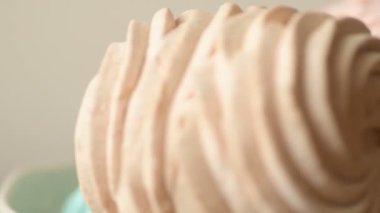 Tatlı renkli ev yapımı pastel şekerlemeler nane yeşili, pembe ve krema renkleri seramik plaka üzerinde ağır çekimde dönüyor sarı arka planda şeker tozu serpiştiriliyor. Ev yemeği. 