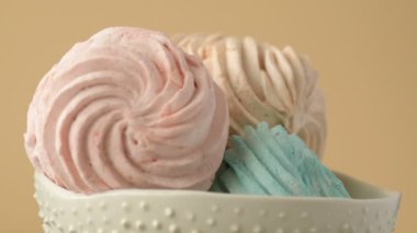 Tatlı renkli ev yapımı pastel şekerlemeler nane yeşili, pembe ve krema renkleri seramik plaka üzerinde ağır çekimde dönüyor sarı arka planda şeker tozu serpiştiriliyor. Ev yemeği. 
