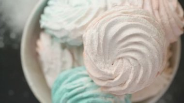 Tatlı renkli ev yapımı pastel şekerlemeler nane yeşili, pembe ve krema renkleri seramik plaka üzerinde ağır çekimde dönüyor sarı arka planda şeker tozu serpiştiriliyor. Ev yemeği. 