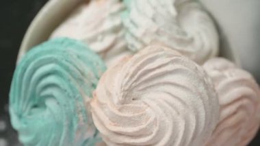 Tatlı renkli ev yapımı pastel şekerlemeler nane yeşili, pembe ve krema renkleri seramik plaka üzerinde ağır çekimde dönüyor sarı arka planda şeker tozu serpiştiriliyor. Ev yemeği. 