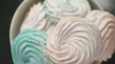 Tatlı renkli ev yapımı pastel şekerlemeler nane yeşili, pembe ve krema renkleri seramik plaka üzerinde ağır çekimde dönüyor sarı arka planda şeker tozu serpiştiriliyor. Yukarıdan görüntüle