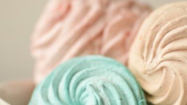 Tatlı renkli ev yapımı pastel şekerlemeler nane yeşili, pembe ve krema renkleri seramik plaka üzerinde ağır çekimde dönüyor sarı arka planda şeker tozu serpiştiriliyor. Yukarıdan görüntüle