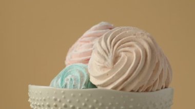 Tatlı renkli ev yapımı pastel şekerlemeler nane yeşili, pembe ve krema renkleri seramik plaka üzerinde ağır çekimde dönüyor sarı arka planda şeker tozu serpiştiriliyor. Ev yemeği. 