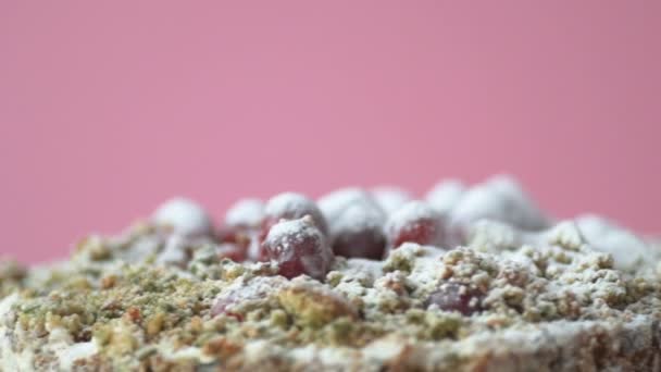 クランベリーで装飾されたほうれん草と自家製のビーガンケーキはゆっくりと回転し ピンクの背景に砂糖の粉を振りかける取得 健康的なベジタリアンや自家製食品のコンセプト — ストック動画
