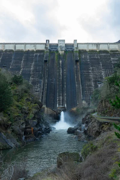 Presa do Bao (Bao Barajı) 'nın büyük beton duvarında hava durumu, yosun ve karanlık çizgiler görülüyor. Alt kapaktan bir su püskürtüsü salınıyor. İspanya 'nın Galiçya kentindeki yaşlanan hidroelektrik altyapısı ve su yönetimi