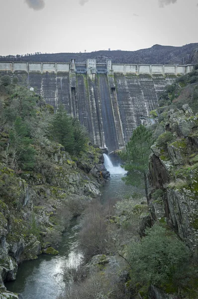 Yıpranmış bir hidroelektrik barajındaki su boşaltma borusunun yakın plan detayları. Beton duvar, koyu su lekeleri, yosun büyümesi ve aşınma ile birlikte ciddi yaşlanma belirtileri gösteriyor. Altyapı bakım sorunlarını resmediyor