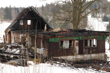 Bir ağacın arka planında, karda yanmış bir ev.