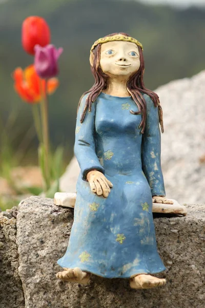 Mavi elbiseli seramik peri lalelerin yanındaki bahçede oturuyor.