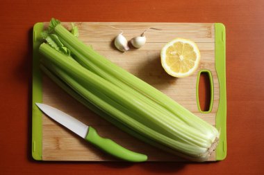 Kereviz saplı mutfak tahtası, limon, sarımsak ve yeşil bıçaklı.