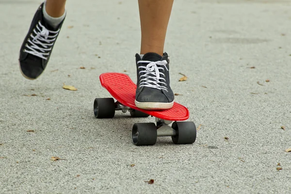 Skater bewegt sich auf einem roten Skateboard mit schwarzen Turnschuhen auf einer Teerstraße — Stockfoto