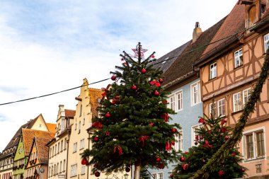 Almanya 'nın Bavyera eyaletinde Rothenburg ob der Tauber' de bir sokakta kırmızı kurdele ve süslemelerle süslenmiş güzel bir Noel ağacı. Arka planda renkli geleneksel evlerin olduğu şenlikli tatil sahnesi.