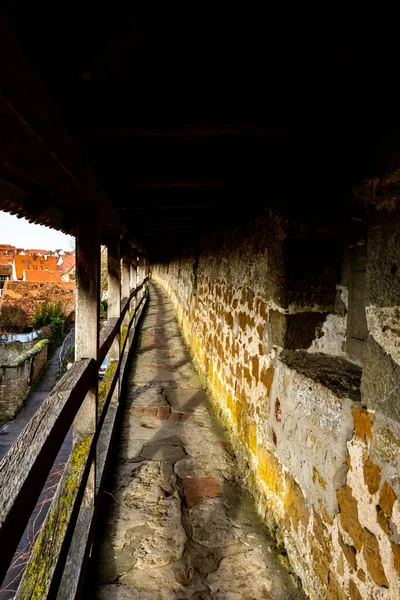 Historic covered walkway inside the old city wall of Rothenburg ob der Tauber, Bavaria, Germany. Medieval stone fortifications with wooden roof and battlements, famous tourist attraction and UNESCO heritage site. Vertical photo