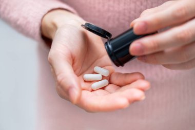 Tanımlanamayan bir kadının elinde ilaç tutarken çekilmiş yakın plan fotoğrafı. Sağlık ve tıbbi konsept. Evinde ya da ofisinde elinde üç beyaz hap tutan bir kadın.. 