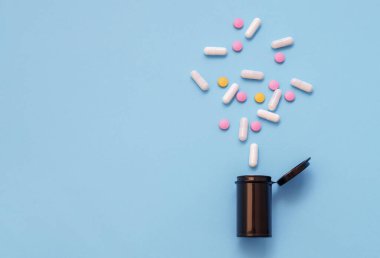 Opioid salgını, ağrı kesiciler ve uyuşturucu bağımlılığı konsepti. Bir şişe reçeteli ilaç ve hidrokodon hapının mavi arka planda düşmesi.. 