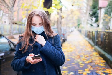 Sokaklarda cep telefonunu kullanarak alışveriş yapan mutlu bir kadının portresi, yaşam tarzı kavramları. Kadın, Coronavirus covid-19 salgını sırasında açık havada tekrar kullanılabilir maske takıyor. Kendine dikkat et..