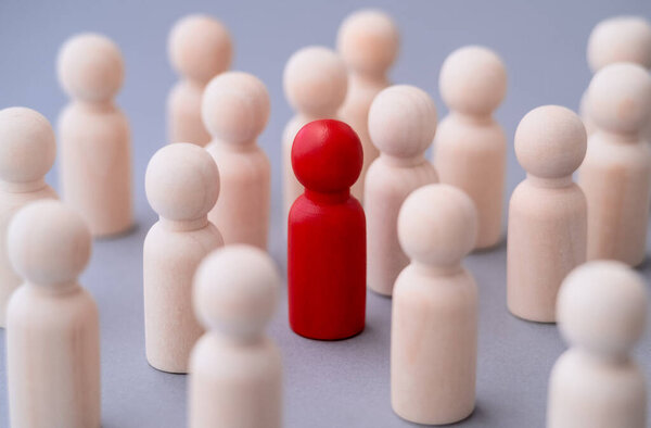 Red figure of a man made of wood, standing out from the crowd of. Different people. Unique human shape among light ones. Leadership, individuality and standing out of crowd concept